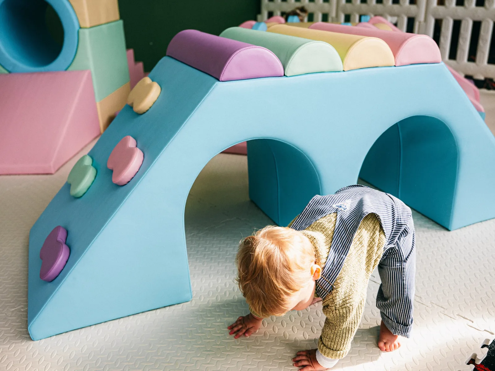 A toddler playing under a pastel soft play arch inside a Joyful Little Spaces set up