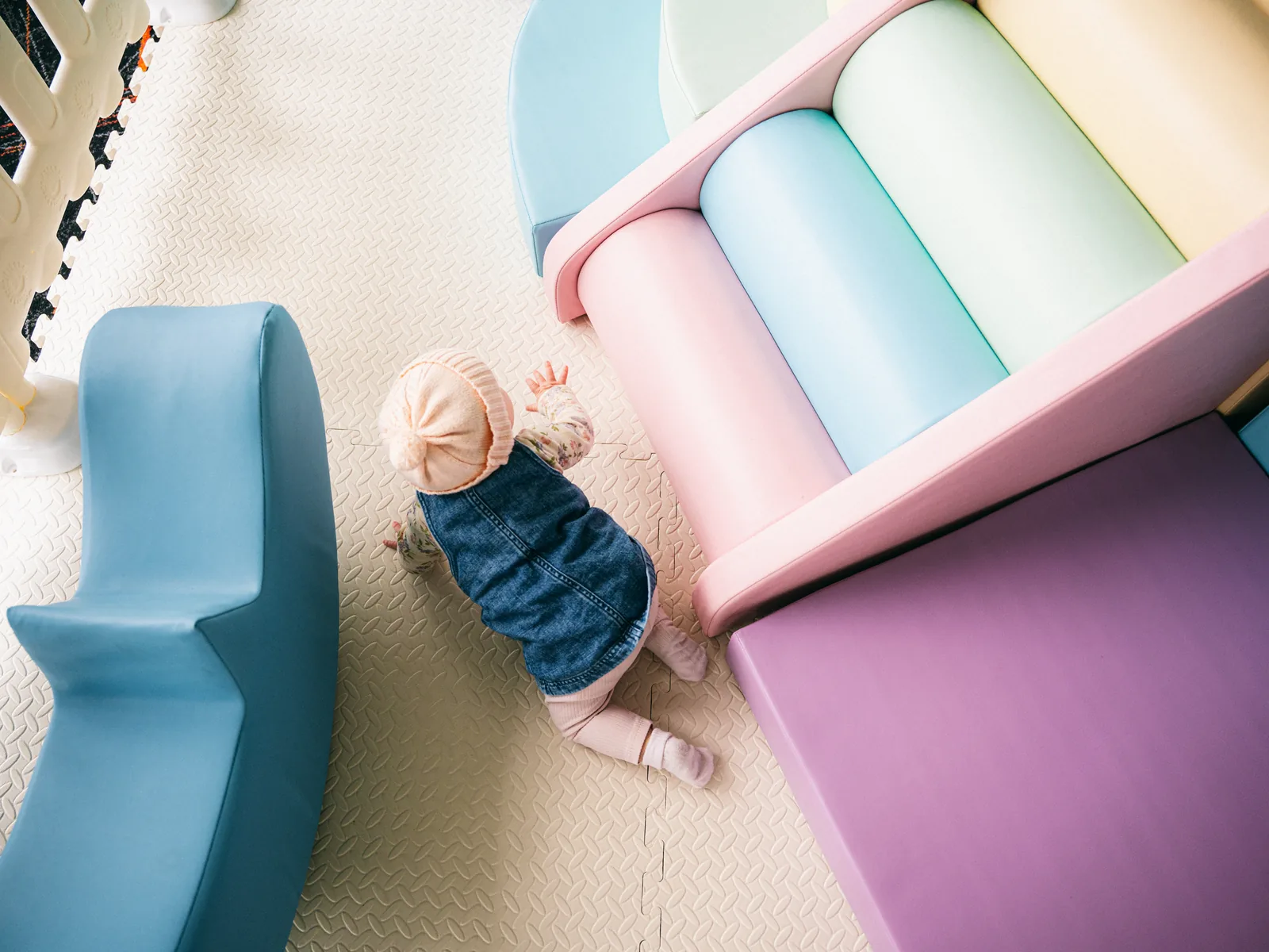 A baby crawling beside pastel soft play blocks and a rocker on padded matting